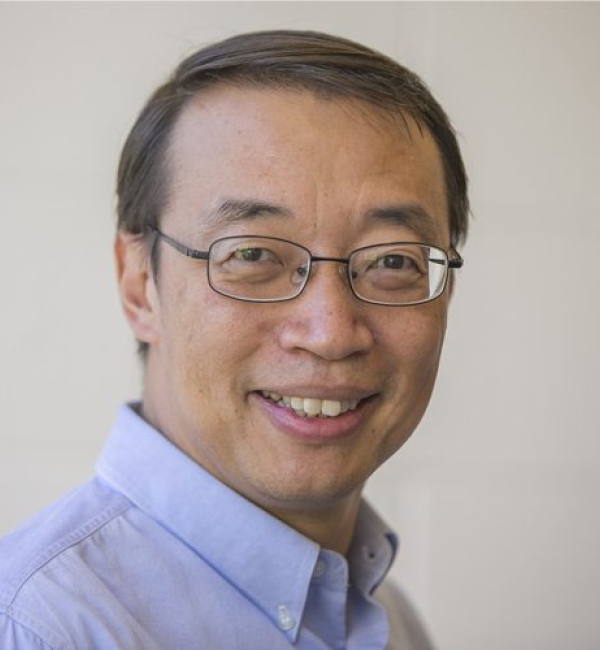 Chris Xu smiling at the camera wearing a lavender collared shirt.