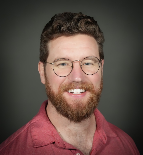 A headshot of a man with dark hair and glasses