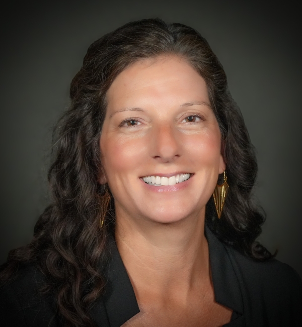 A headshot of a woman with brown hair on a gray background. 