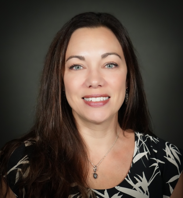 A headshot of a woman with brown hair on a gray background. 