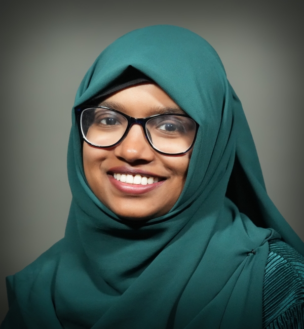 A headshot of a woman with black glasses on a gray background. 