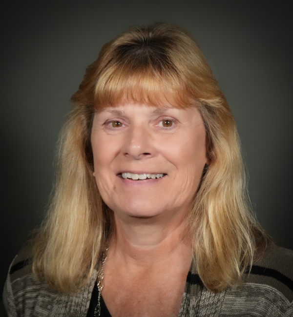 A headshot of a woman with blonde hair on a gray background. 