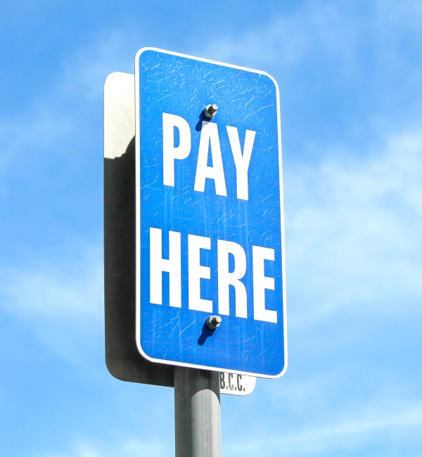 A blue "PAY HERE" sign with white lettering is mounted on a pole against a clear blue sky.