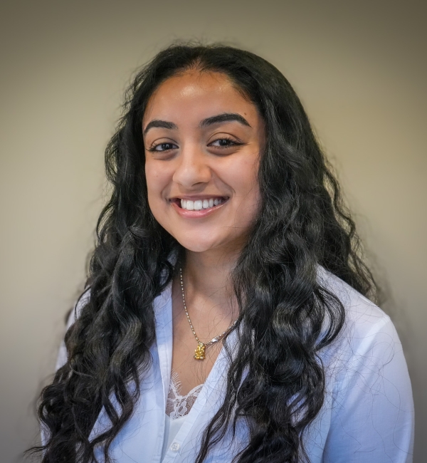 A woman with dark hair in front of a light wall. 