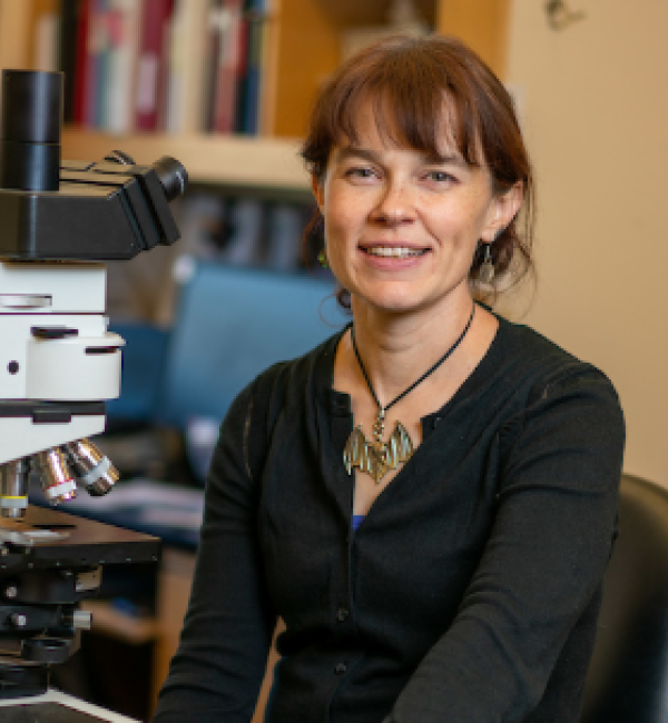 Photograph of Dr. Teri Orr smiling at the camera and sitting in front of a microscope.