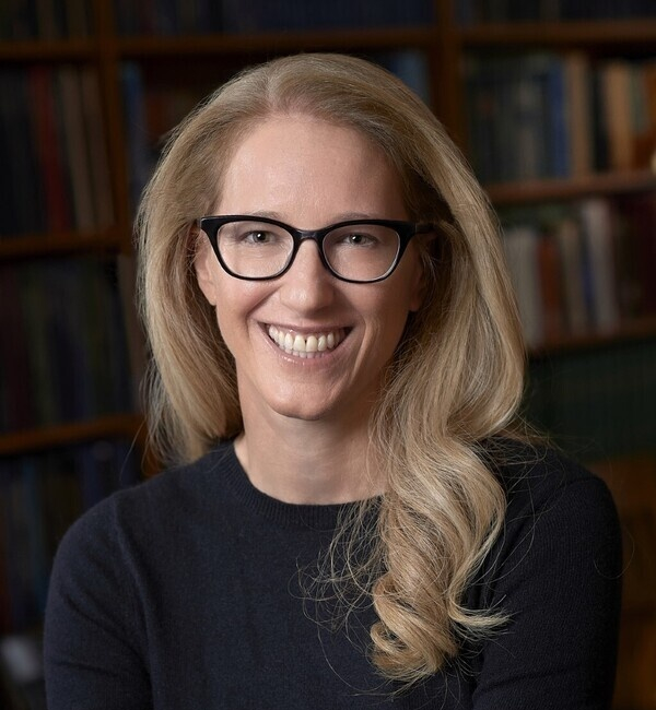 Raina Plowright sitting in front of a bookcase wearing a black long-sleeved shirt.