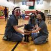 three students sitting around a black dog