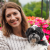 Stephanie Coco with a fluffy white dog seated outdoors near flowering bushes