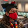 A veterinary student in a cap and gown with a mask on listens to the keynote speaker at the college's send-off ceremony