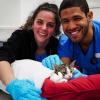 Students smile at the camera while assisting a cat during spay day