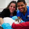 Students smile at the camera while assisting a cat during spay day