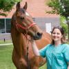 Michelle Delco in scrubs next to a brown horse outside of the college