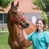 Michelle Delco in scrubs next to a brown horse outside of the college