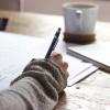 Stock image of a person in a sweater at a writing desk, with papers and a mug before them