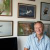 David Russell stands in front of a wall of his wildlife photographs